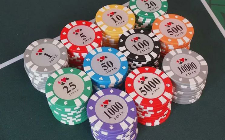 Zestaw żetonów pokerowych w różnych kolorach — białe, czerwone, zielone, czarne, fioletowe — z widocznymi nominałami